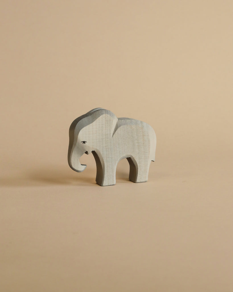 A Ostheimer Small Elephant - Eating figurine stands against a plain beige background, showcasing its stylized shape and subtle wood grain texture.