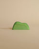 A small, green, minimalist handcrafted Ostheimer Bush shaped like a hill, placed against a plain beige background.