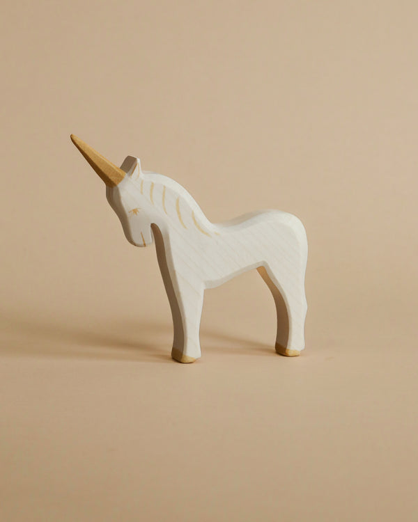 A handcrafted Ostheimer Unicorn with a natural finish stands on a beige background. The unicorn features painted eyes and a simple, stylized horn.