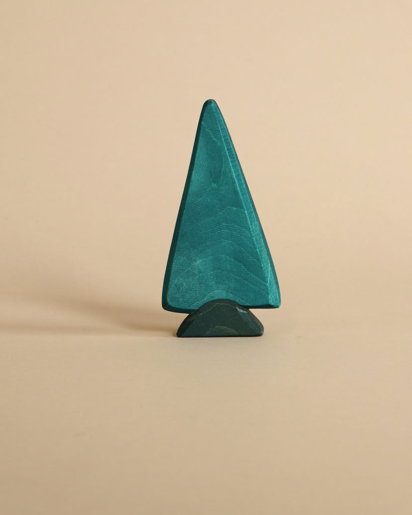 A teal, handcrafted Ostheimer Spruce Tree figurine stands against a light beige background, showcasing a simple and minimalist design.