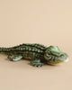 A realistic plush model of an Alligator Stuffed Animal lying down on a plain beige background. The figure is highly detailed, capturing even the textures of its scales.