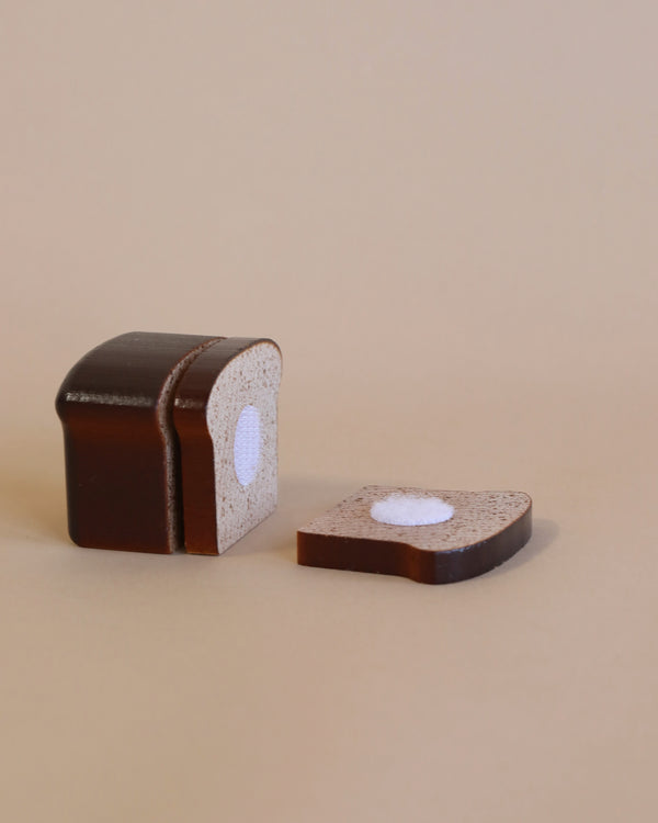 A loaf of bread styled as a chocolate cake, with one slice cut by Erzi Bread to Cut Pretend Food, revealing a white, round center on a light beige background.