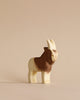 A Handmade Holzwald Goat with detailed, two-tone fur pattern and realistic features, standing against a plain, light beige background. This high-quality piece is part of our sustainable toys collection.