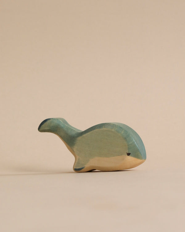 A high-quality, handmade Handmade Holzwald Whale toy, painted in shades of green and tan, on a plain beige background.