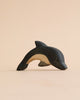 A high-quality Handmade Holzwald Dolphin figurine with a smooth finish, displayed against a soft peach background. Its colors transition from dark blue to white, emphasizing its curved shape.