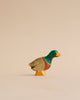 A colorful Handmade Holzwald Male Duck figurine, showcasing shades of green, orange, and beige, stands elegantly against a plain, light beige background. This high-quality wooden toy is both charming and durable.