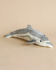 A Dolphin Stuffed Animal with realistic features and a soft gray and white color scheme, lying on a plain light beige background.