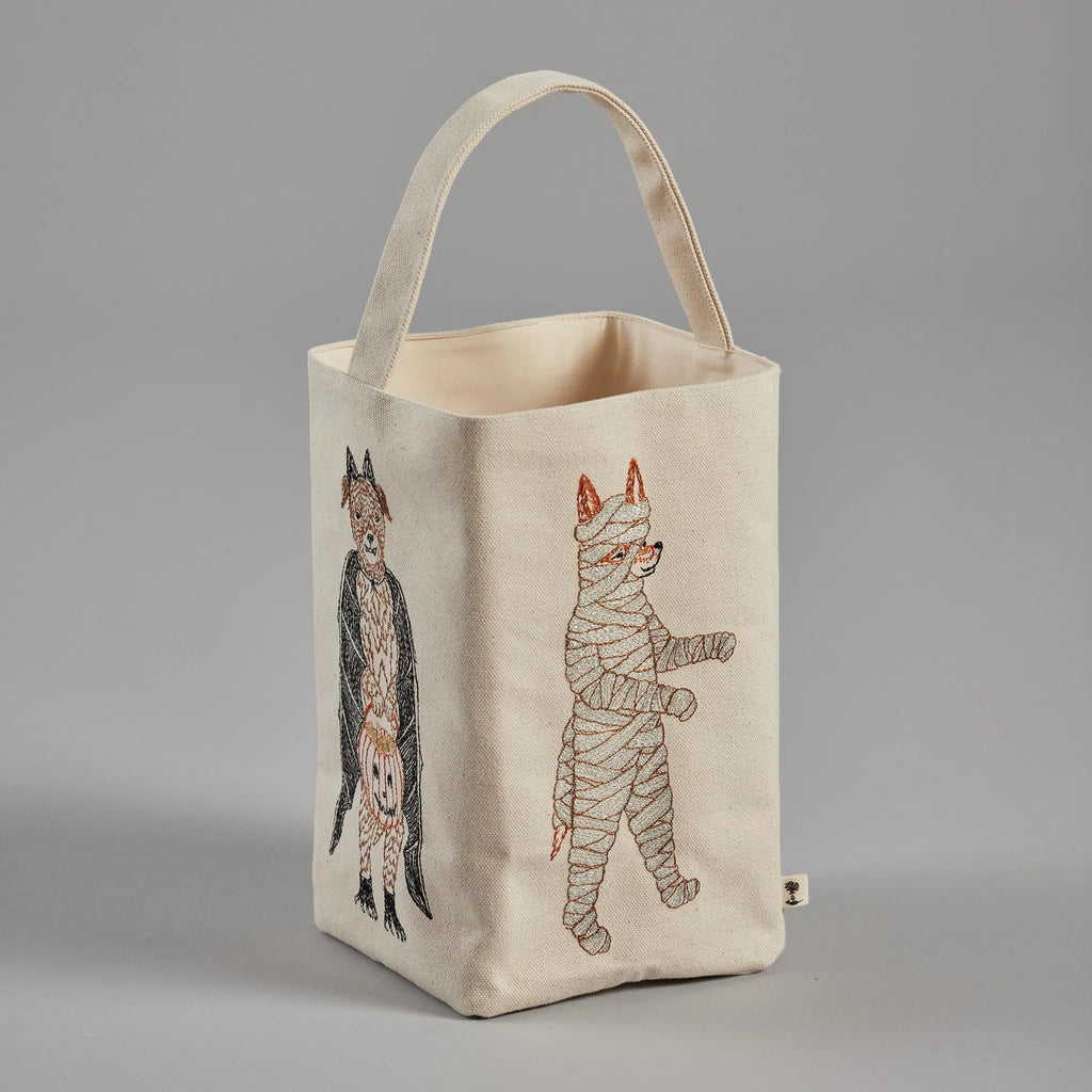 Displayed is the Coral & Tusk Halloween Costumes Bag, a rectangular canvas Trick-or-Treat bag with a handle. The bag showcases embroidered Halloween designs featuring costumed critters—a cat dressed as a bat and another as a mummy—in orange, black, and brown hues against a gray background.