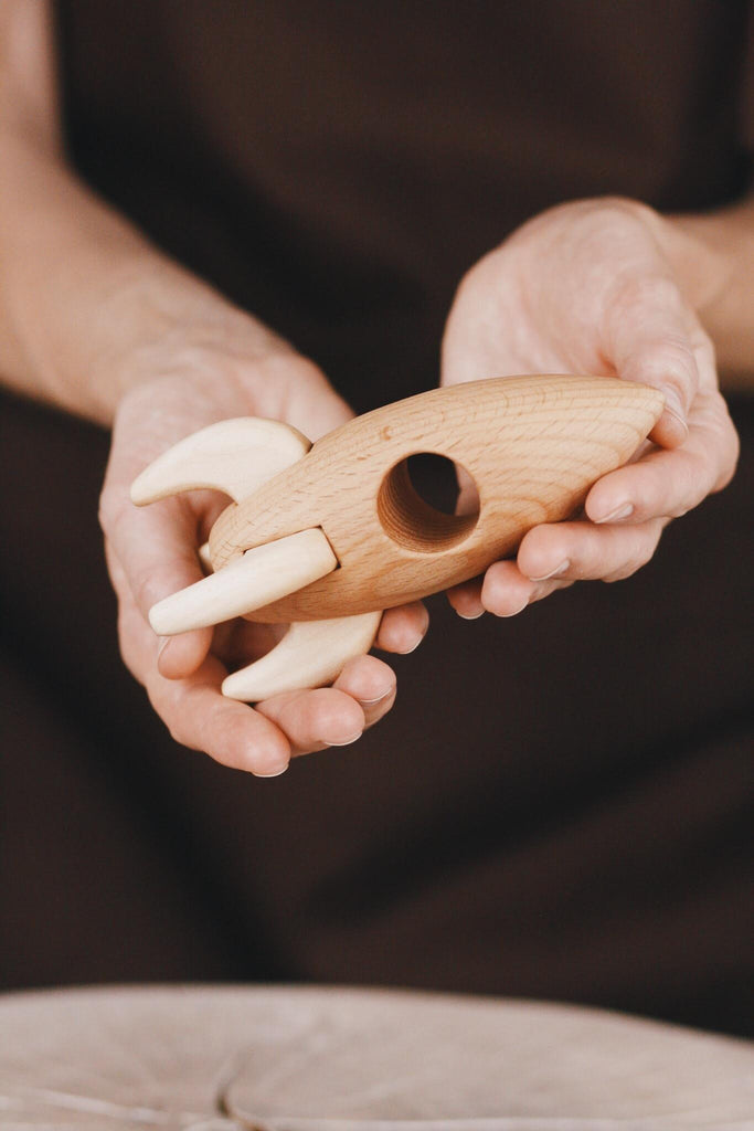 A person holding the Handmade Wooden Rocket, skillfully carved from smooth beech wood and elegantly finished with a gentle coat of linseed oil.