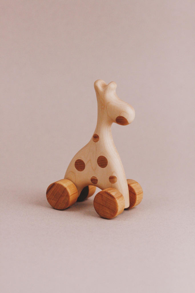 The Handmade Wooden Mini Giraffe Push Toy, crafted from maple and beech wood, boasts a smooth finish with charming brown spots as it stands proudly against a neutral background.