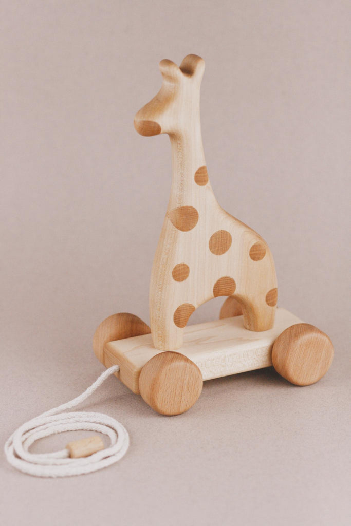 The Handmade Wooden Giraffe Pull Toy is an enchanting children's toy made from handcrafted wood, decorated with playful polka dots. It rolls smoothly on four round wheels and includes a white cord for easy pulling, all set against a neutral beige background to offer endless fun for little ones.