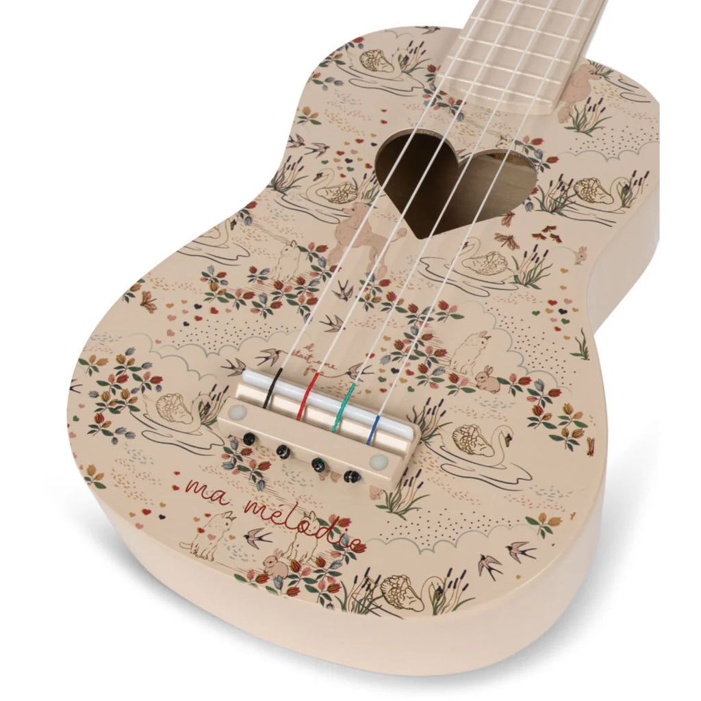 The Konges Sløjd - Wooden Ukulele - Mizumi features a beige, wooden body beautifully adorned with floral and swan patterns. A heart-shaped sound hole lends additional charm, accompanied by the elegant inscription "ma mélodie." This FSC-certified piece combines aesthetic elegance with a commitment to environmental sustainability.