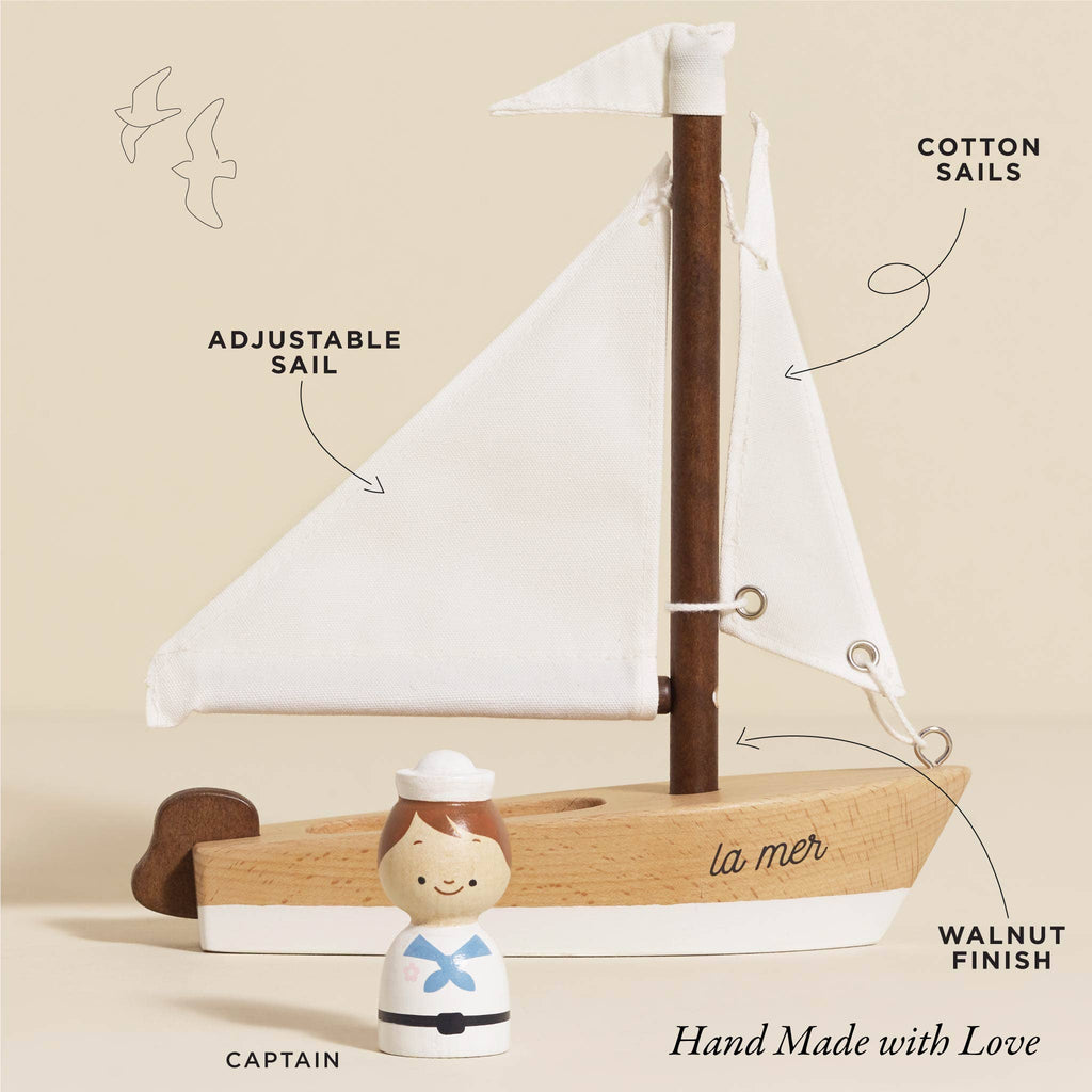 The Wooden Sailing Boat & Captain provides endless imaginative play with its elegant handcrafted design. It features a walnut finish, adjustable white cotton sails labeled "La Mer," and includes a small wooden captain dressed in sailor attire. The phrase "Hand Made with Love" is charmingly accented by whimsical seagull illustrations.