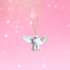 A Gold and White Snowy Owl Necklace with a pendant shaped like an owl with wings spread wide, adorned with 24k gold-plated accents. The background is a soft, bokeh pink gradient, creating a dreamy and whimsical atmosphere.