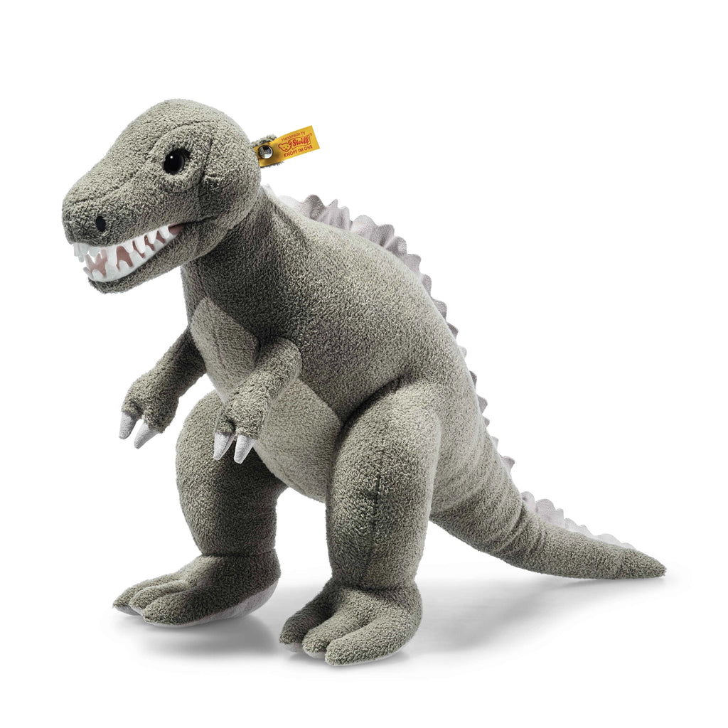 A gray Steiff, Thaisen Tyrannosaurus "T-Rex" Dinosaur Plush Toy, 18 Inches with a tag on its head, featuring white sharp teeth, small round black eyes, and spiky ridges along its back. The dinosaur is in a standing position with its arms and legs slightly bent.