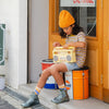 A young girl in a striped yellow t-shirt and blue shorts sits on a colorful drum outside a store, absorbed in using the Retro Wooden Tape Recorder. She wears a yellow beanie and grey boots.