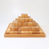 A Grimm's Large Natural Stepped Pyramid made of 100 building blocks, arranged in a tiered fashion. It sits on a square wooden base, with the blocks becoming gradually smaller towards the top, creating a stepped pyramid shape. The background is plain white.