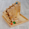 A Grimm's Large Natural Stepped Pyramid with a staircase design and varying block heights is mounted on a wooden tray. Three rubber balls in green, orange, and blue are positioned in different areas, with the blue ball on a higher level and the green and orange balls at the base.