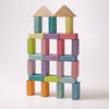 The Pastel Duo Block Set creates a vibrant structure composed of wooden toy blocks in various pastel shades such as pink, blue, green, yellow, and orange. The geometric shapes combine to form a building crowned with two triangular roof pieces. This delightful assembly is part of the Pastel Duo collection and is displayed against a plain white background.