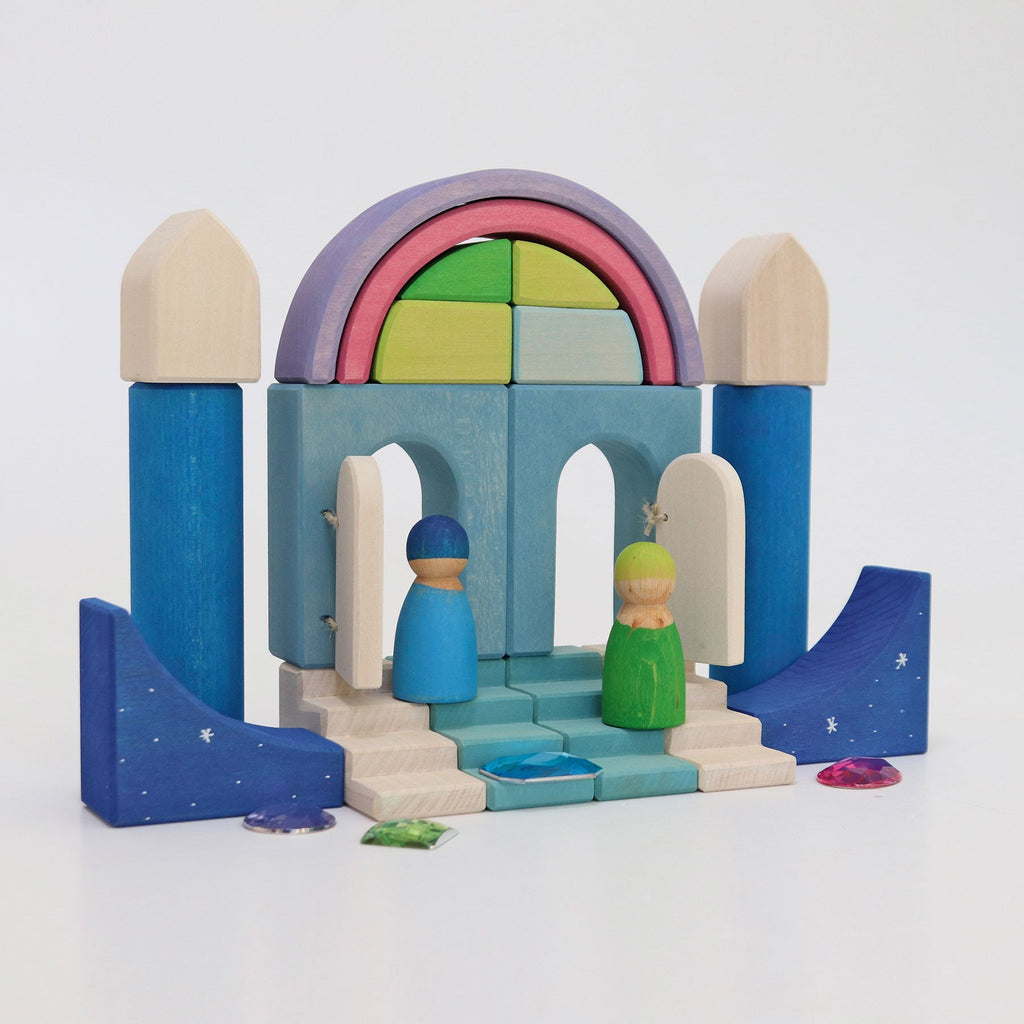 A Grimm's Building World Polar Light Block Set with blue pillars, a multicolored arch, and open doors. Two wooden peg figures, one blue and one green, stand on the steps. Decorative blue blocks with star patterns and colorful gem-like pieces are on the ground. Set against a white background, it’s perfect for small Play Worlds.