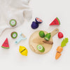 The Wooden Chopping Board & Sliceable Play Food set offers a lively and colorful collection of wooden toy fruits and vegetables such as kiwi, watermelon, and carrot. Ideal for role play, it comes with a toy knife designed to enhance fine motor skills. Set against a white background with a nearby striped cloth, this playset is perfect for sparking imaginative play.