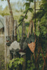 Three Donsje Chaeso Purses in Carrots, Walnut Nubuck, and Tan colors hanging on rustic wooden posts surrounded by lush green foliage.