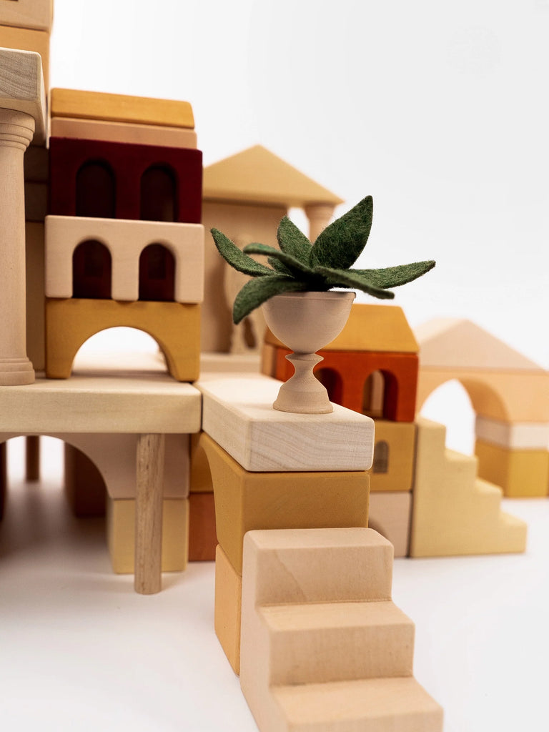 A close-up of a small green felt plant in a silver pot, meticulously placed on a Sabo Concept Italian Ancient City Blocks, set against a plain white background.