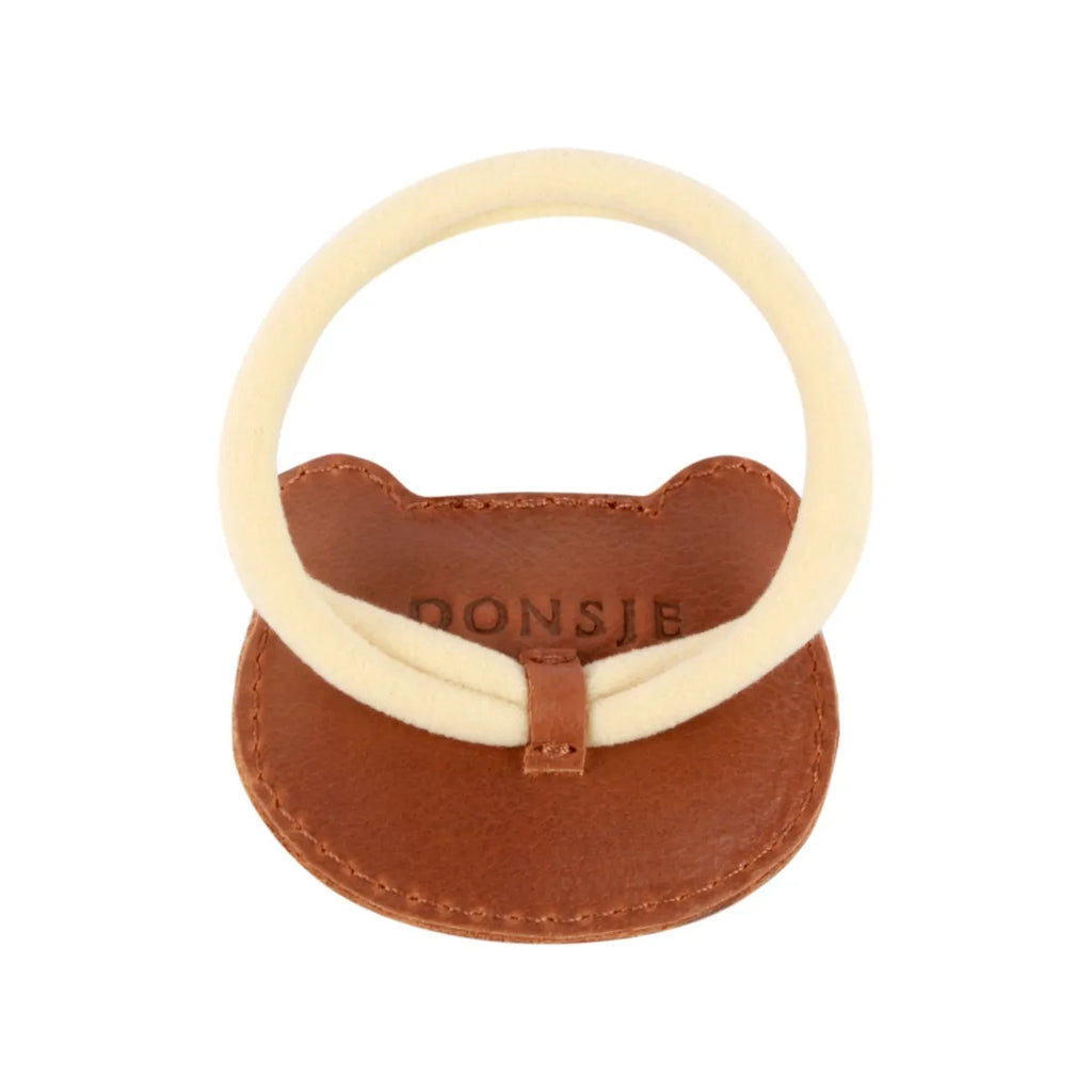 A children's teething ring featuring a light tan circular silicone ring attached to a brown Donsje Leather Hair Tie - Bear holder with the brand name "donsje" stamped on it.