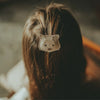 A close-up of a person's hair adorned with the charming Donsje Leather Hair Tie, which is shaped like a cat's face. This cute accessory, crafted from premium leather, complements the softly blurred background as the person sits serenely.