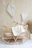 A cozy nursery scene featuring a light-colored wicker bassinet with a soft, polyester blanket draped over the side. The background wall is adorned with two fluffy Boucle Kite Wall Decors in cream and a string of pom-poms, adding a whimsical touch to the children's room decoration. Pampas grass in a vase complements the decor.