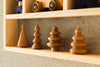 A Wooden Shelf No. 21 displays four handcrafted wooden Christmas tree decorations and a toy train. Each tree boasts a unique design, from simple geometric shapes to intricate layered forms. Set against a textured wall, this charming scene makes for perfect storage shelves in children's rooms.