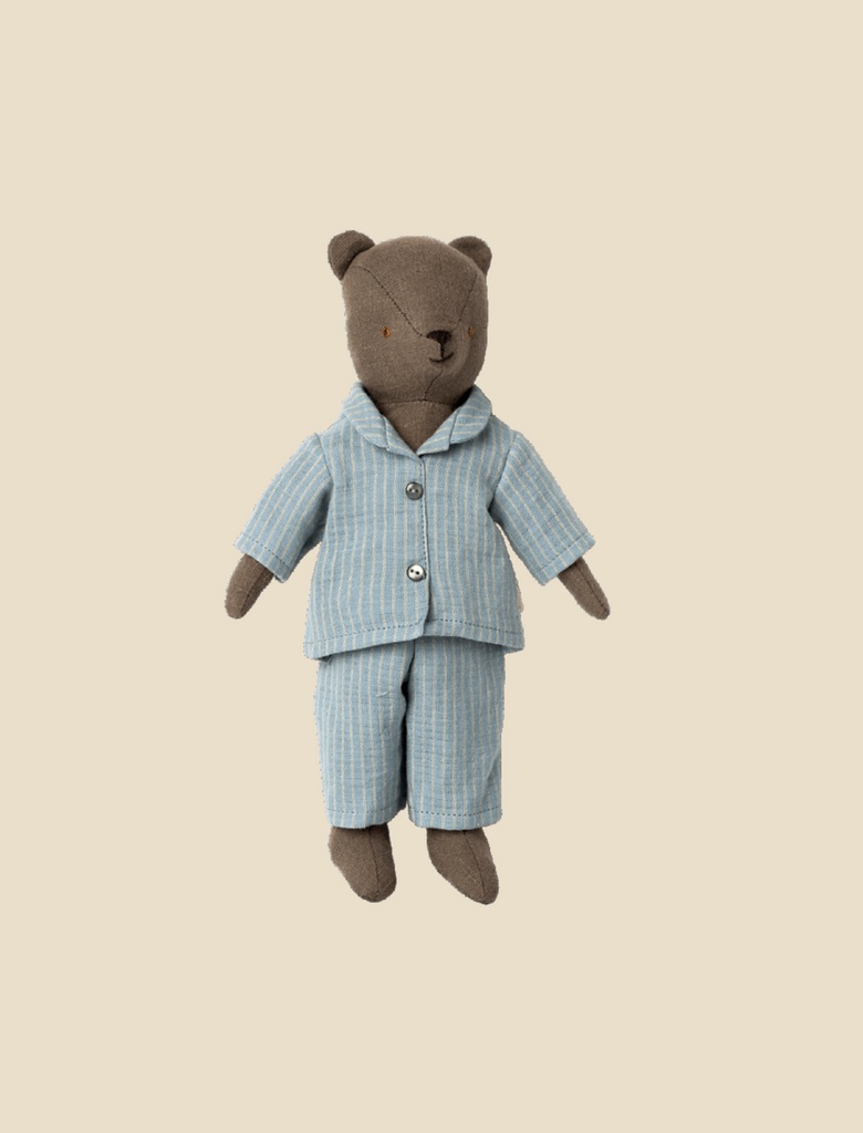 A brown teddy bear named Teddy Dad is dressed in light blue, striped pajamas and stands upright against a plain beige background. This adorable look can be yours with the Maileg Extra Clothing: Pyjama for Teddy Dad, which is available for purchase separately.