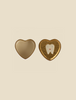 Two heart-shaped containers on a light beige background. The container on the left is open and empty, evoking childhood memories, while the one on the right is closed and features a white tooth with a smiley face on a golden background, perfect as a Maileg Tooth Box.