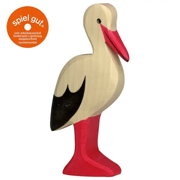 A handcrafted wooden toy stork stands upright with red legs and beak, a white body, and black wings. There’s an orange "spiel gut" recommendation sticker in the top left corner. This beautiful piece is part of the renowned Holztiger Stork collection, proudly made in Europe.