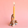 A whimsical holder shaped like a sitting giraffe with a detailed pattern, crafted from fine porcelain, features a lit twisted yellow candle. The background is bright pink, making this heirloom-quality Giraffe Cake Topper truly stand out.