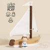 Displayed is the Wooden Sailing Boat & Captain, a beautifully crafted wooden toy with a white sail and a small sailor figurine. The backdrop showcases illustrated text: "Learn, Discover, Play," along with icons representing cognitive skills, imagination, dexterity, and coordination.