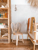 A cozy corner of a room featuring two Toddler Rattan Bunny Chairs facing a beige wall with an adjacent woven rack displaying various colorful spools of thread, and a wooden rack with blankets and hanging decorations.