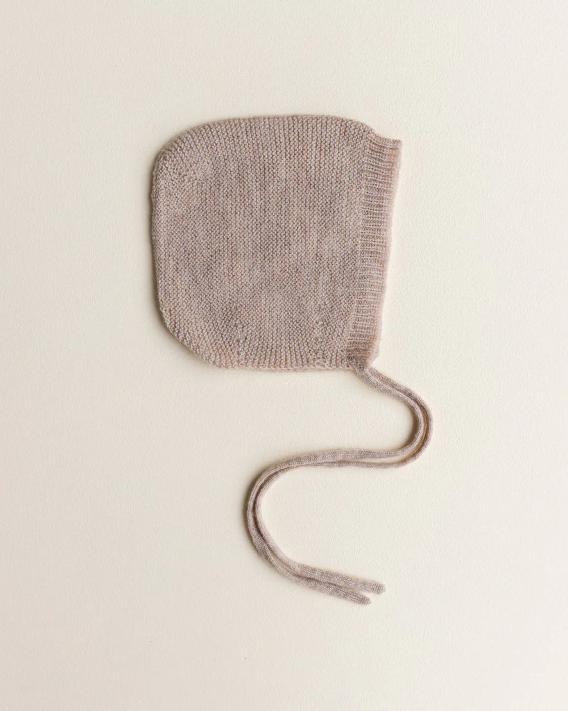 A single Handmade Merino Wool Newborn Bonnet in Sand, made of extra fine Italian merino wool, with long ties, placed against a plain light background.