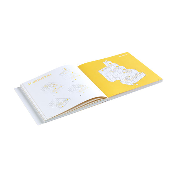 Sentence with product name: An open book with yellow and white pages displaying geometric illustrations and text titled "standard 90", including Cuboro The Book. The book is on a plain white background.