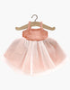 A diminutive, sleeveless ballet dress featuring a gentle pink bodice and a light, airy white tulle skirt, hanging on a wooden hanger against a simple backdrop—exquisitely crafted in France as the Rosella Tutu in Marsala for Minikane dolls.