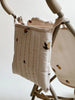 A close-up of a padded, quilted bag hanging from a beige Konges Sloejd Doll Stroller - Lemon frame. The bag is cream-colored with a pattern of small, illustrated lemons and leaves. The background is plain and white, highlighting the stroller's double wheels for added stability.