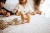 A small Handmade Wooden Horse figurine handcrafted from linden wood stands on a table, surrounded by scattered bits of food, paper egg cartons, and other wooden toys painted with child-safe paint. Two children, slightly blurred in the background, are engaged in an activity.