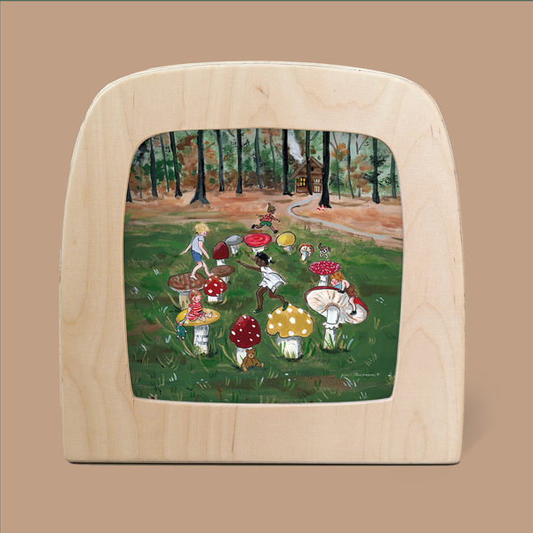 A whimsical painted scene on wood, titled "Silhouette Only - Toadstool Dance Silhouette for Toverlux Lamp," features children in colorful outfits twirling around oversized mushrooms in a forest setting. A small house peeks through the trees, framed by natural wood, capturing the essence of Magic Silhouettes.