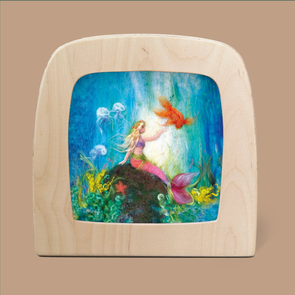 Introducing "Silhouette Only - Underwater World for Toverlux Lamp": This enchanting artwork captures a mermaid perched on a rock in an underwater realm, extending her arm towards a large orange fish. The lively scene is enriched with mystical silhouettes of sea plants and jellyfish. It comes beautifully framed in a decorative wooden frame with curved edges, showcased against a neutral backdrop.