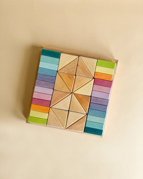 The Pastel Duo Block Set features a square puzzle composed of colorful wooden blocks, meticulously arranged in an intricate pattern. These blocks, evoking soft pastel duo shades, include a spectrum of hues such as blue, purple, red, orange, green, and natural wood tones. The set incorporates geometric shapes like triangles and rectangles to create symmetrical designs.