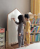 Two children in pajamas use the NORITER Signature Double-Sided Board Bundle to draw with magnetic alphabets in a cozy room. The space, adorned with pastel-toned crates and a bookcase filled with vibrant books, is made even warmer by a plaid curtain in the background.