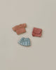 A set of Maileg Extra Clothing: Clothes & Bag for Big Sister - Old Rose, featuring a small doll outfit with an orange and brown striped short-sleeve shirt, a blue and white plaid skirt, and a pink crossbody bag, is neatly arranged on a plain beige background.