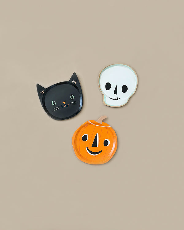 Meri Meri It's Halloween! Plates feature a vintage look with a beige background, including designs of a black cat face, an orange jack-o'-lantern, and a white skull face with black eyes and nose.