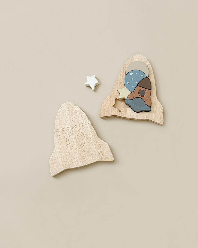 A light-colored beechwood Wooden Puzzle - Rocket is displayed on a beige background. The top section has been removed to reveal pieces shaped like a blue astronaut helmet and a brown spaceship. A small white star piece lies above the puzzle, all crafted from FSC-certified wood.