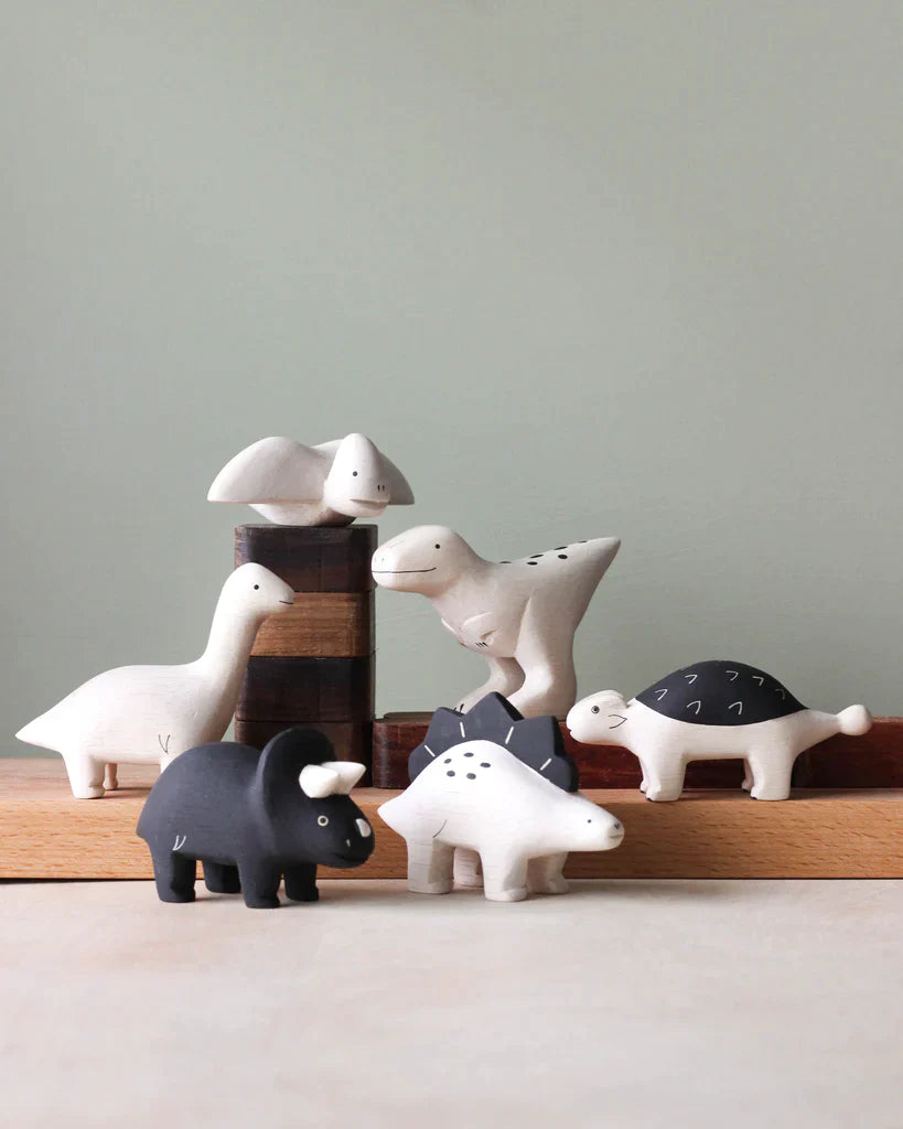 A collection of Handmade Tiny Wooden Dinosaurs - Triceratops displayed against a pale green background.